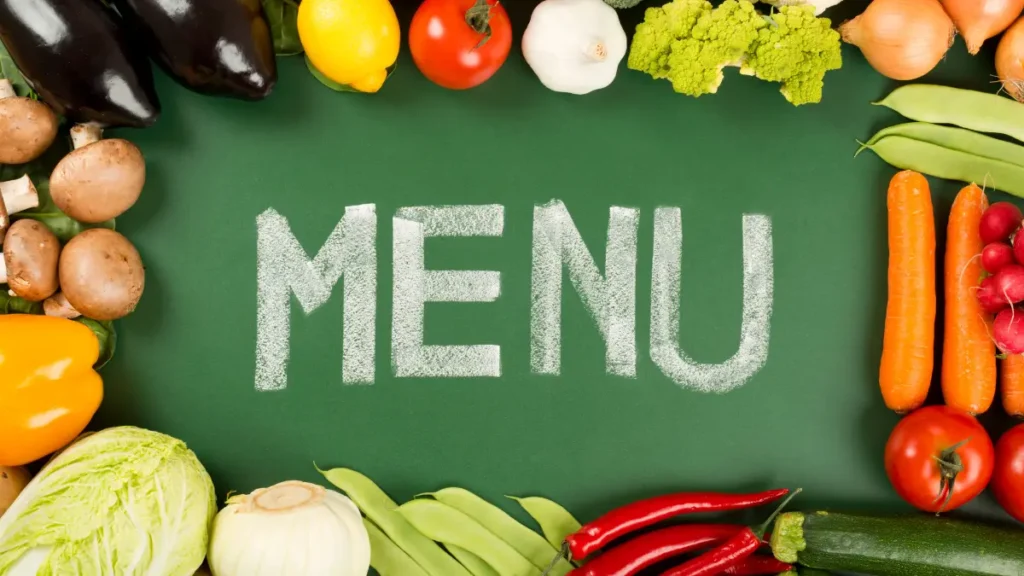 A colorful array of vegetables, including eggplants, tomatoes, and carrots, frame the word "Newk's Eatery Hattiesburg Menu" written in chalk on a green chalkboard background.